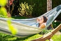 Young girl relaxing having nap in hammock in garden at home at bright sunny day. Slow living, gadget detox