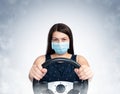 Young girl in a respiratory mask driving a car, front view.