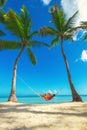 Young girl resting in a hammock under tall palm trees, tropical beach Royalty Free Stock Photo