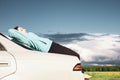 A young girl resting on the trunk of a car against the backdrop of an incipient thunderstorm, during a long journey on a suburban