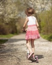 Young girl riding scooter away from camera on path through park Royalty Free Stock Photo