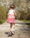 Young girl riding scooter away from camera on path through park Royalty Free Stock Photo