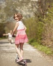 Young girl riding scooter in park away from camera to mother Royalty Free Stock Photo