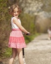 Young girl riding scooter in park away from camera to mother Royalty Free Stock Photo