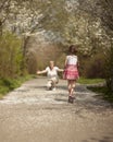 Young girl riding scooter in park away from camera to mother Royalty Free Stock Photo