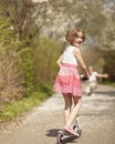 Young girl riding scooter in park away from camera to mother Royalty Free Stock Photo