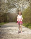 Young girl riding scooter on path through park Royalty Free Stock Photo