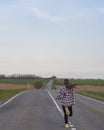 A young girl runs along the road. A girl with long blond hair runs away alone on a deserted road that goes into the distance among Royalty Free Stock Photo