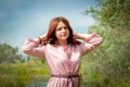 A young girl, Russian, in a Slavic costume, stands in a summer park with her hands behind her head