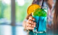 Young girl`s hand holding a glass with a blue lemonade cocktail with fruits