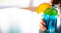 Young girl`s hand holding a glass with a blue lemonade cocktail with fruits at a table Royalty Free Stock Photo