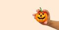 A young girl`s hand holds a small orange pumpkin for Halloween against the background of the color trend #FAEBD7 Champagne 2021. A Royalty Free Stock Photo