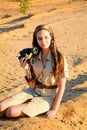 A young girl in safari style clothes sits on the golden sand with binoculars in her hands. Portrait Royalty Free Stock Photo