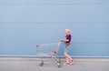 Young girl with shopping carts walking down the street on the background of a turquoise wall Royalty Free Stock Photo