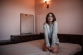 A young girl in a short skirt and a white blouse sits on the bed with a sad and thoughtful face Royalty Free Stock Photo