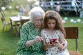 Young girl showing something on smartphone to elderly grandmother at garden party. Love and closeness between