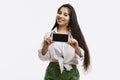 Young girl shows a blank screen smartphone. Beautiful bright brunette with long hair in a white shirt and green shorts. White Royalty Free Stock Photo