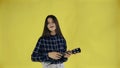 Young girl singing and playing ukulele on yellow Background in Studio Royalty Free Stock Photo