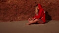 Young girl sit in yoga pose on the wet sand of the shore near clay mountain, by the sea