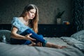 Young girl sits on a bed in her room, holds her injured leg with her hand Royalty Free Stock Photo