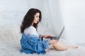 A young girl sits on a bedand uses a laptop. Indoors in the bedroom. Royalty Free Stock Photo