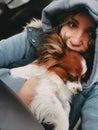 A young girl sits in a car in a blue jacket and a hood and holds a sleeping dog in her arms Royalty Free Stock Photo