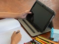 young girl sits at her desk, colorful array of pencils scattered around her.Beside her notebook,tablet beckons, its screen filled