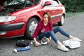 A young girl sits near a broken car and makes repairs to the electric generator, next to her there are bad parts, tools and first Royalty Free Stock Photo