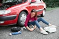 A young girl sits near a broken car and makes repairs to the electric generator, next to her there are bad parts, tools and first Royalty Free Stock Photo