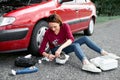 A young girl sits near a broken car and makes repairs to the electric generator, next to her there are bad parts, tools and first Royalty Free Stock Photo