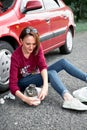 A young girl sits near a broken car and makes repairs to the electric generator, next to her there are bad parts, tools and first Royalty Free Stock Photo