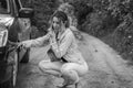 A young girl sits near a car with a broken wheel on the road and calls the rescue service to have her car repaired Royalty Free Stock Photo