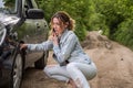 A young girl sits near a car with a broken wheel on the road and calls the rescue service to have her car repaired Royalty Free Stock Photo