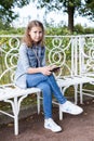 Young girl sits on steel white bench in park, holds smartphone for chatting, looking at camera Royalty Free Stock Photo