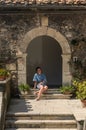 A young girl sits on the steps near the entrance to an old antique house in a small Italian town Royalty Free Stock Photo