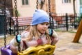 A young girl sits on a swing in a playground, her expression is thoughtful and introspective.