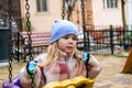 A young girl sits on a swing in a playground, her expression is thoughtful and introspective.