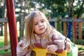 A young girl sits on a swing in a retro-styled playground, her expression is thoughtful and introspective.