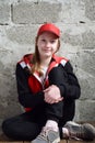 Young girl is sitting in black sports suit, red cap and smiling. Concept portrait of a pleasant friendly happy teenager