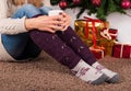 Young girl sitting on carpet floor and holding cup of coffee in hands on legs with warmers and Christmas tree and gift boxes in ba Royalty Free Stock Photo