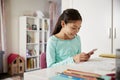 Young Girl Sitting At Desk In Bedroom Using Mobile Phone Whilst Doing Homework Royalty Free Stock Photo