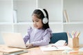 A young girl is sitting at a desk with a laptop and headphones on Royalty Free Stock Photo