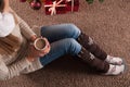Young girl sitting on floor on carpet with cup of coffee in hand and next to Christmas gifts box Royalty Free Stock Photo