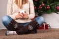 Young girl sitting on floor and holding cup of coffee, in background is Christmas tree and present box Royalty Free Stock Photo