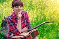 Young girl sitting on the grass in the field and plays the guitar. Beautiful nature at bright sunny summer day.