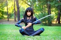 Young girl sitting on the grass and holding samurai sword. Royalty Free Stock Photo