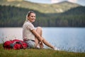 A young girl is sitting beside the lake and posing for a photo during hiking the hills. Trip, nature, hiking