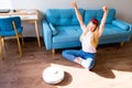 Young girl sitting on the living room floor and enjoying the robot vacuum cleaner. Housework and technology concept