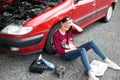 A young girl sitting near a broken car and looking for help, next to her there are bad parts, electric generator, tools and first Royalty Free Stock Photo