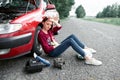 A young girl sitting near a broken car and looking for help, next to her there are bad parts, electric generator, tools and first